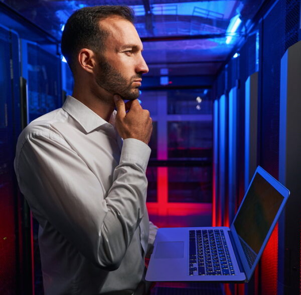 Thoughtful system administrator with laptop in hands looking to the server rack