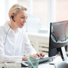 Side view portrait of female hotline operator using laptop and wearing headset while performing customer support service