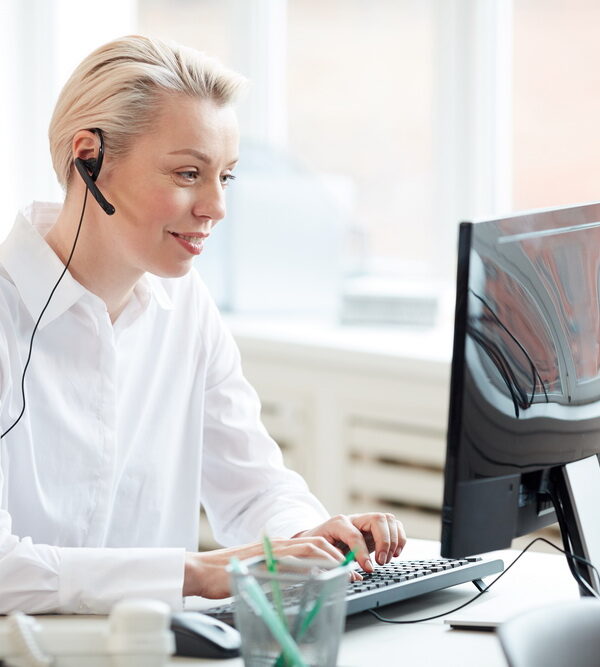 Side view portrait of female hotline operator using laptop and wearing headset while performing customer support service
