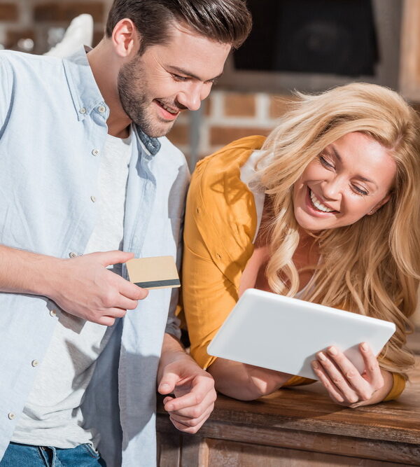 happy beautiful couple making e-shopping with tablet on table at kitchen